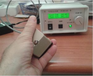 Thermally isolated crystal oven held in hand in front of its temperature controller